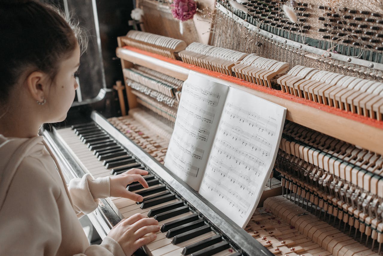 who-we-are A young girl sits indoors playing piano while reading a music sheet, showcasing concentration and musical training.